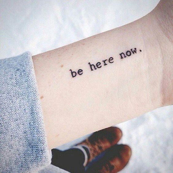 Hình xăm chữ "Be here now" trên cổ tay