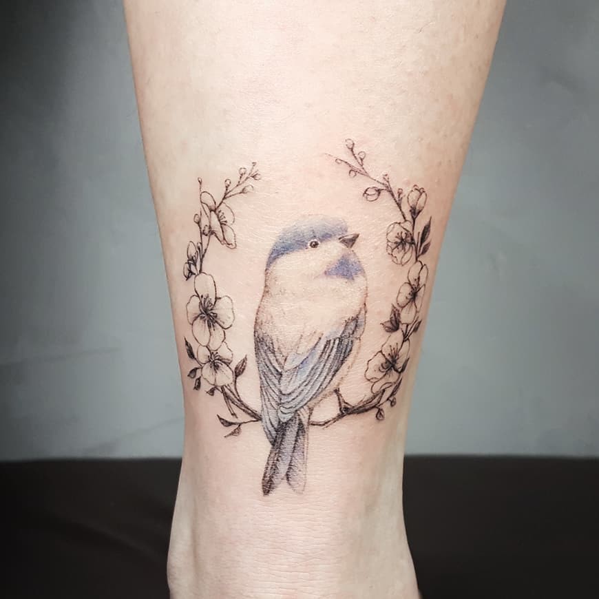 Hình xăm chú chim non đậu trên cành hoa thể hiện sự mong manh, tươi mới
