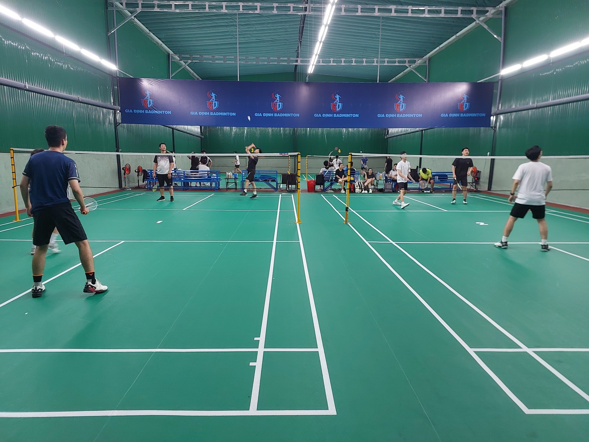 Toàn cảnh một sân cầu lông bên trong nhà với vạch kẻ rõ ràng và khu vực khán giả